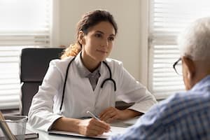 Doctor sitting at desk with papers and pen talking to patient