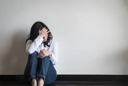 woman sitting on ground against wall suffering from alcohol withdrawal symptoms